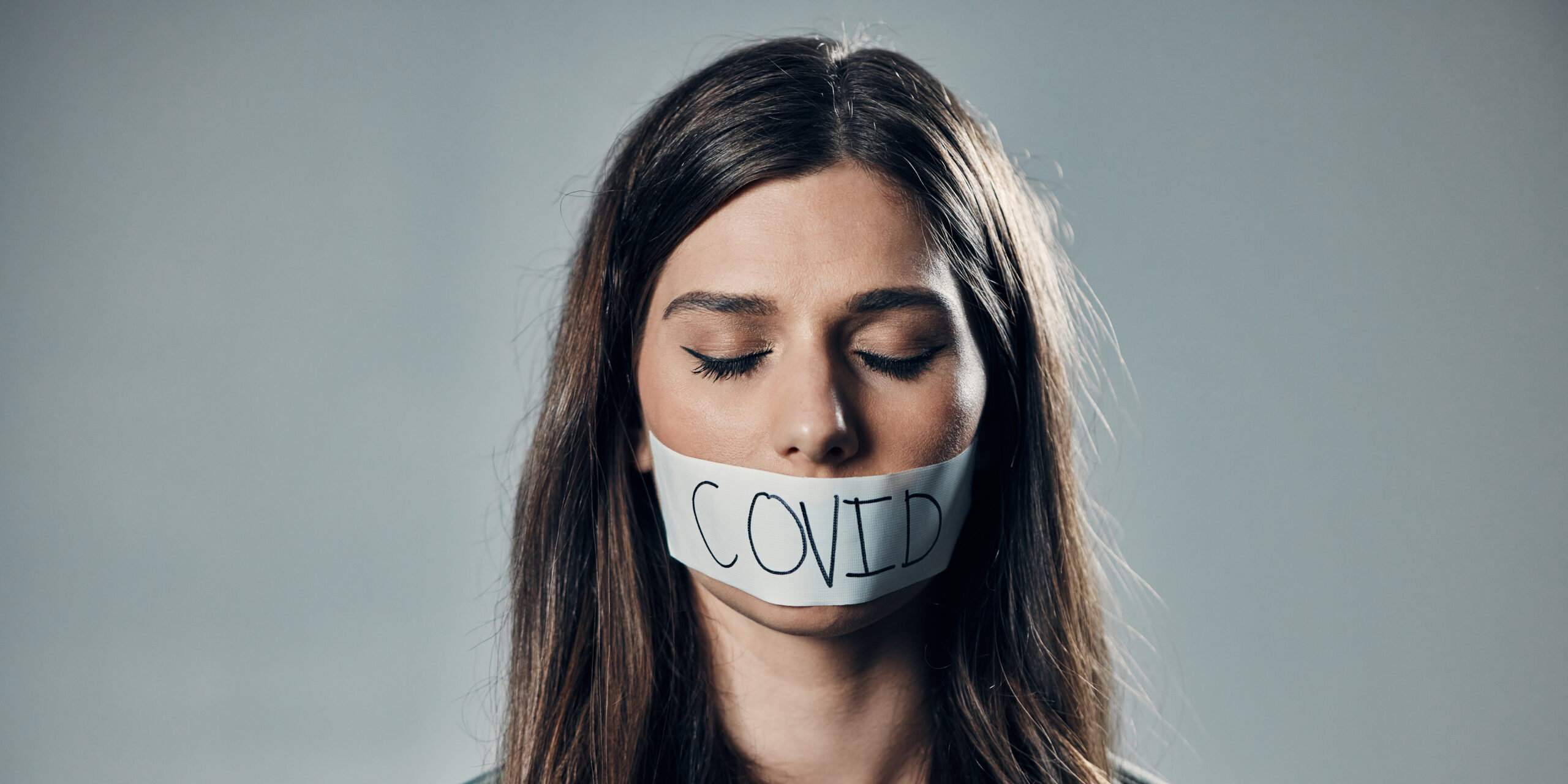 Young woman is silenced by wearing a tape over her mouth bearing the word COVID.