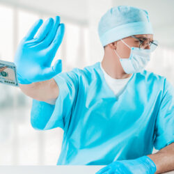 Male doctor in scrubs holds up his hand to refuse cash being handed to him | Article on Stark Law enforcement | Vanguard Communications | Denver