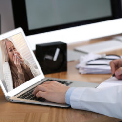 Doctor using proper netiquette for telehealth at laptop with a sick patient on the screen | Vanguard Communications | Denver, CO | San Jose, CA
