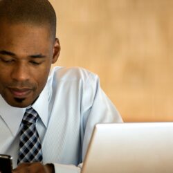 Skilled physicians and computers | Vanguard Communications | Man on smartphone by laptop