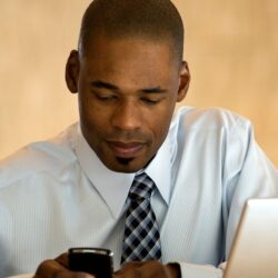 Skilled physicians and computers | Vanguard Communications | Man on smartphone by laptop
